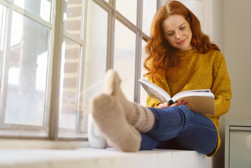 Une femme devant sa baie vitrée en train de lire