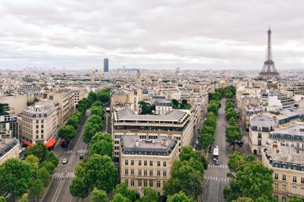 Paris, avec une vue aérienne emblématique où on aperçoit la Tour Eiffel, la Tour Montparnasse et de larges avenues haussmanniennes bordées d’arbres