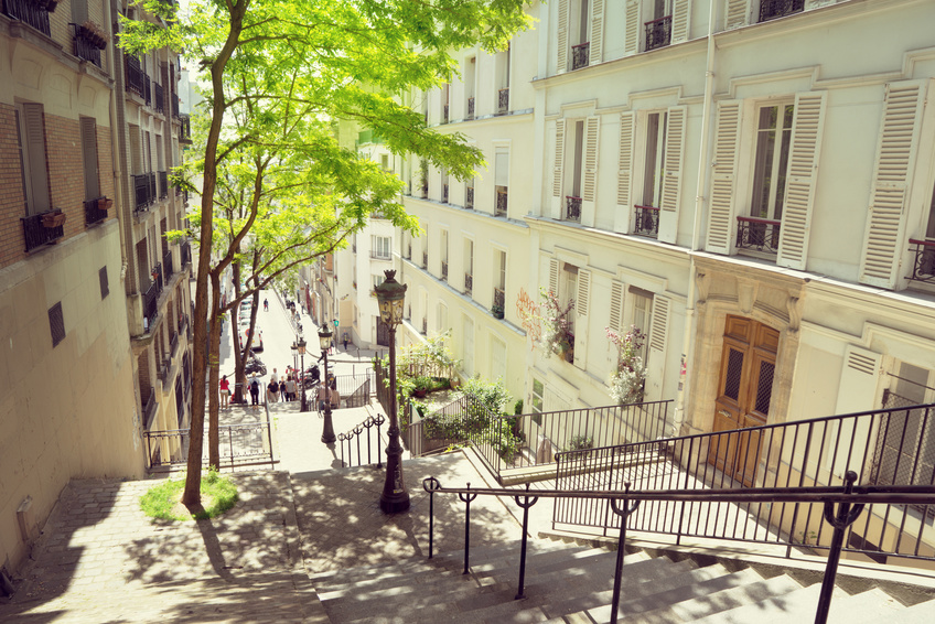 Picturesque staircase in Montmartre, Paris, surrounded by Haussmann-style buildings and bathed in sunlight.