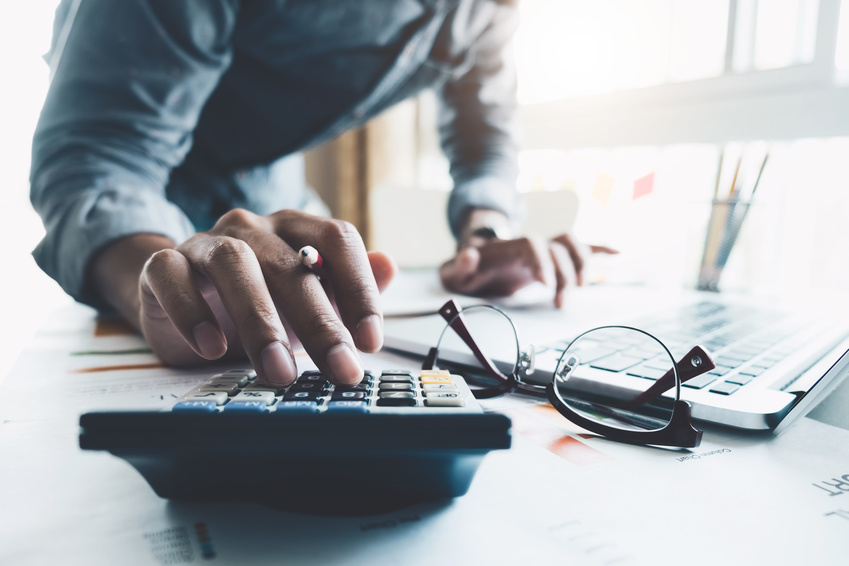 Close up of businessman or accountant hand holding pen working on calculator to calculate business data, accountancy document and laptop computer at office, business concept