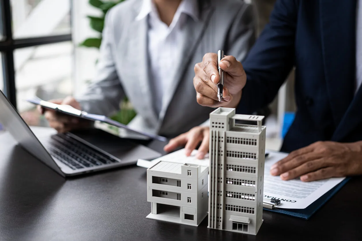 Homme pointant d'un stylo une maquette d'immeuble à côté d'un autre homme tenant un document