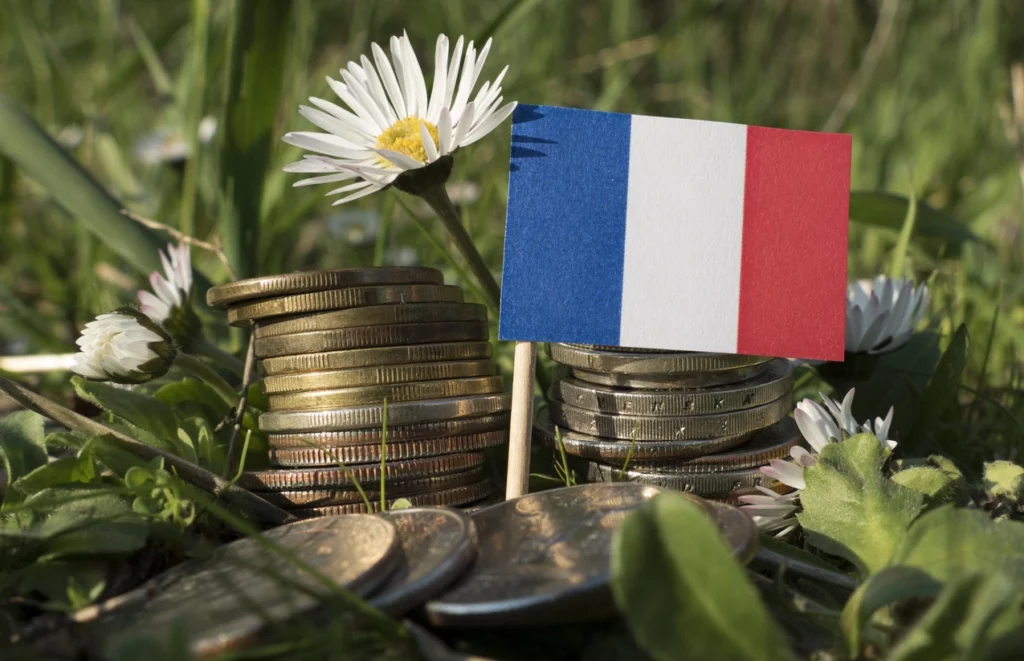 Une image avec un drapeau de France étalée sur des monnaies, montrant l'attrait des investisseurs pour la France.