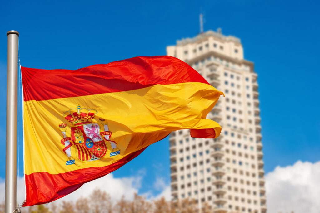 Drapeau espagnol flottant devant un immeuble pour illustrer investir en Espagne